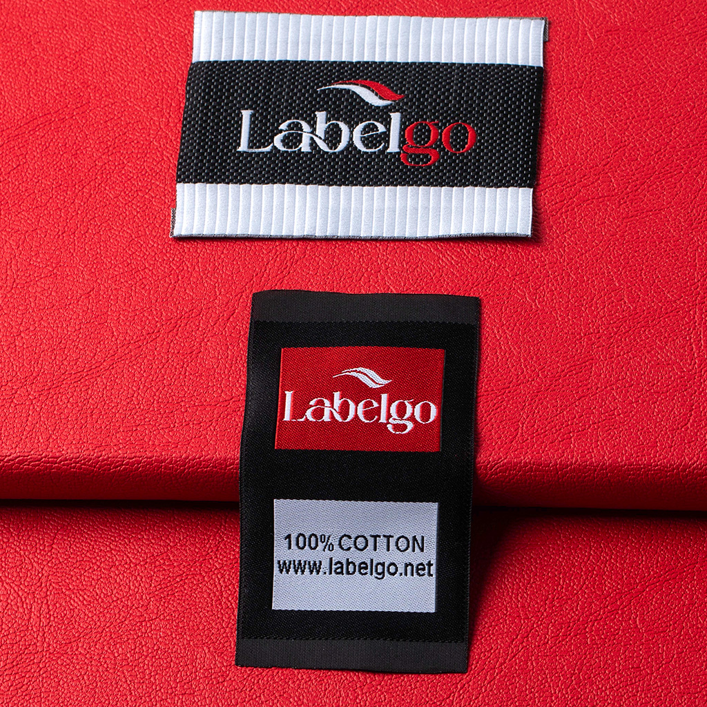 Inquadratura ravvicinata di un'etichetta tessuta nera con logo bianco LabelGo su tessuto rosso.